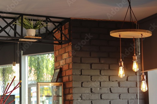 Fototapeta Naklejka Na Ścianę i Meble -  Round lamp in a cafe. Defocused artificial flowerpots on shelves in black metal frames and black, brick walls. Copy space - room design, room interior.