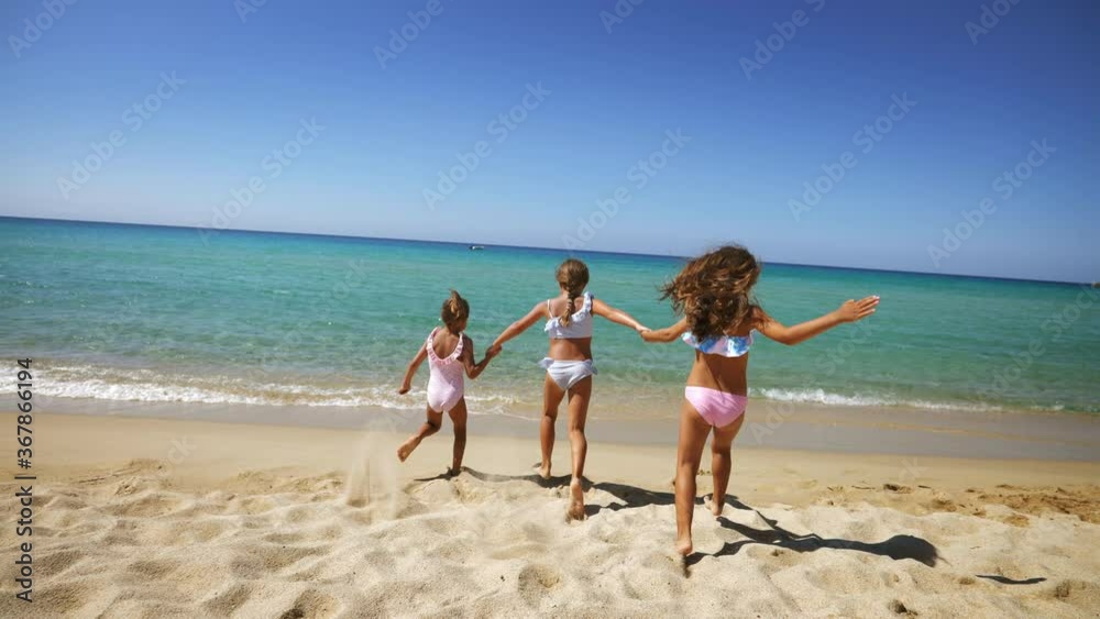 Authentic back view shot of happy healthy little girls are having fun and enjoying to run and splash a water in the sea on a sunny day during family holidays vacation. Authentic back view shot of happy healthy little girls are having fun and enjoying to run and splash a water in the sea on a sunny day during family holidays vacation.