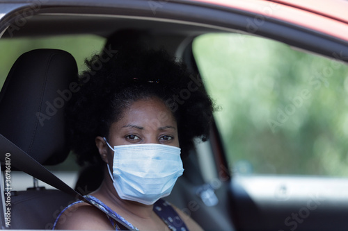 Afro woman looks out the car window while she wears a surgical face mask