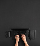 Top view of female hands working on black laptop at dark desk with copy space.