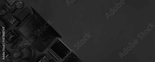 Top view of of photography gear and laptop geometricaly arranged on abstract black background