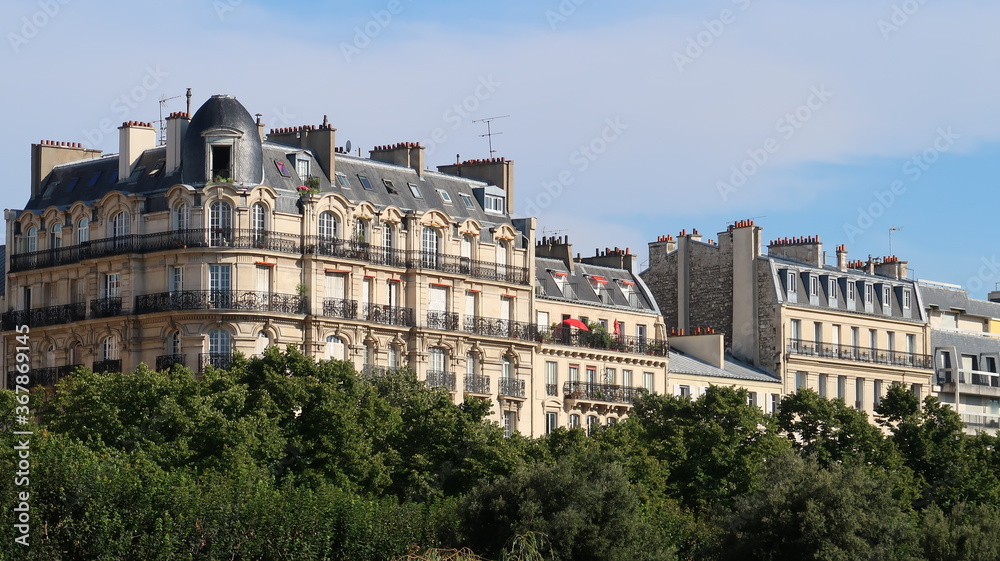Immobilier à Paris, vue sur des immeubles parisiens haussmanniens, émergeant au-dessus des arbres en été (France)