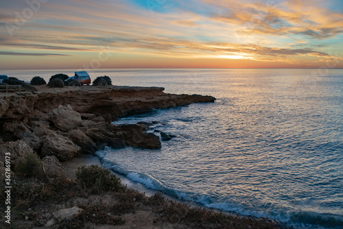 Scenic view of rocks by seascape at beach against sky during sunset