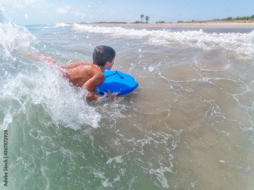 boy bodyboarding on a wave on a deserted beach seen from behind