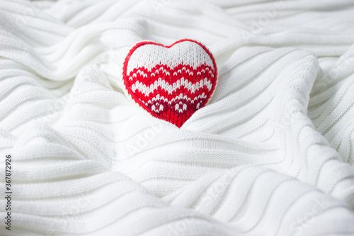 Knitted textile background of white color with heart.