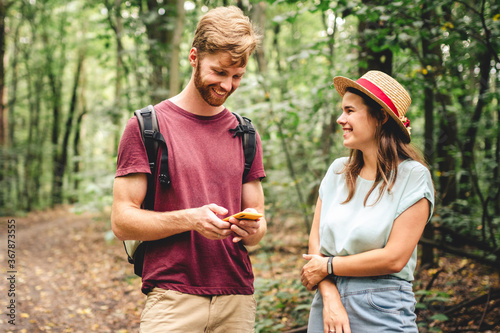 Young caucasian couple uses a smartphone to navigate in the forest. Hiking tourists orientation on the terrain using an online map, an application in a smartphone. GPS for building a route for a walk © Elizaveta