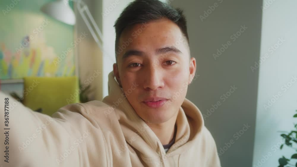smart Asian guy using pov video call communicate with business colleague friend from home during self isolation from coronavirus outbreak crisis. A man wearing headphone looking camera.