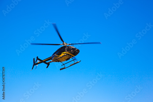 The isolated black yellow helicopter flying in the sky.