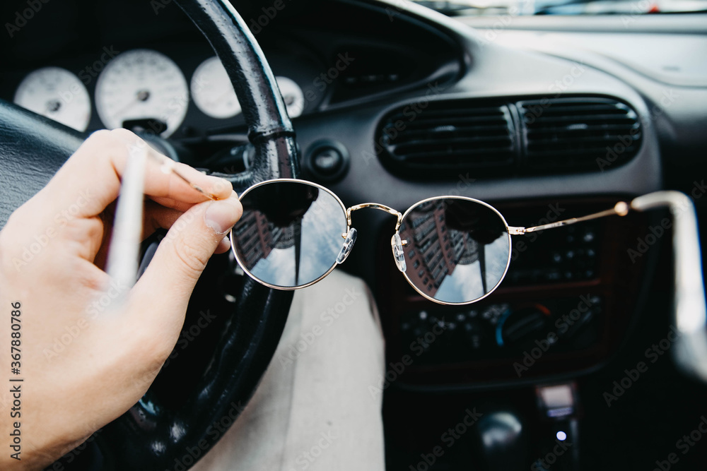 Obraz premium sunglasses in the hands of the driver against the background of the car interior.