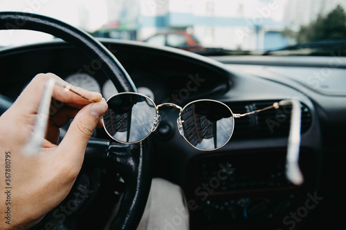 sunglasses in the hands of the driver against the background of the car interior. © velimir