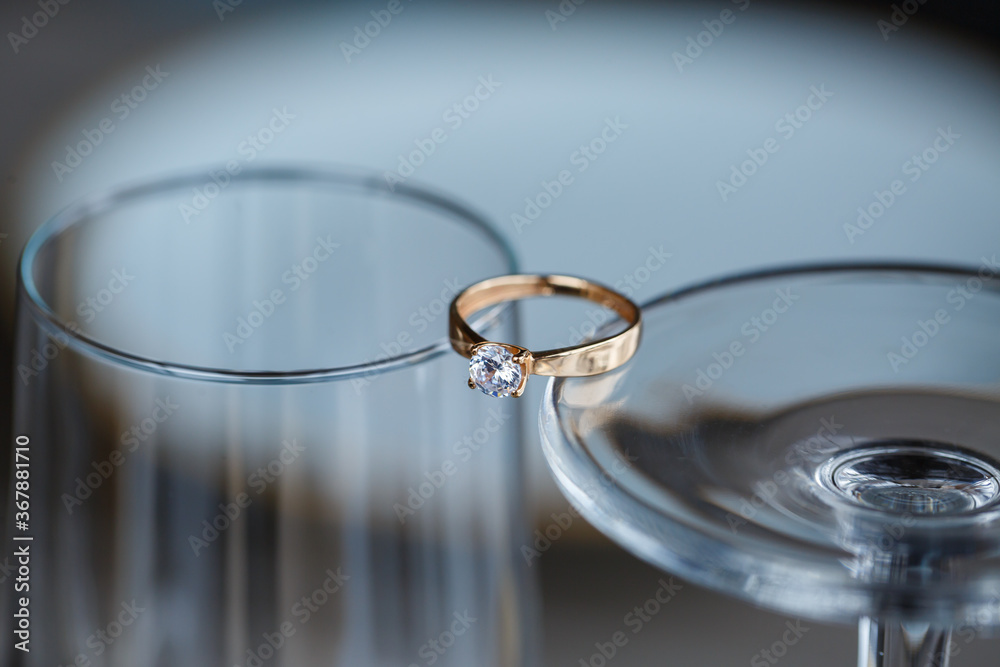 A wedding ring made of precious metal with a diamond stone lies in a glass A wedding ring made of precious metal with a diamond stone lies in a glass