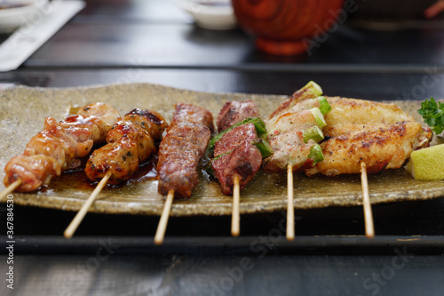 Yakitori, set of Japanese skewers of charcoal grilled meat, beef, pork, beacon and vegetable, serve on plate and wooden table. 