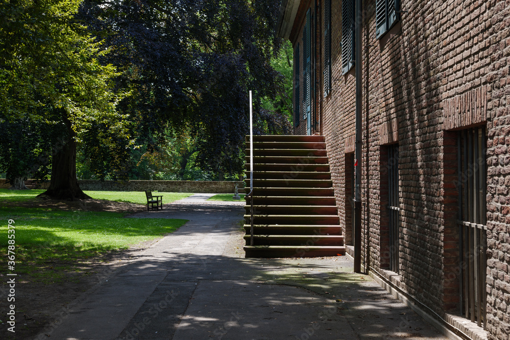 Obraz premium Outdoor sunny and shady scenery around old rough historical brick facade and staircase of Stadtmuseum Düsseldorf and Rosengarten, tranquil garden.