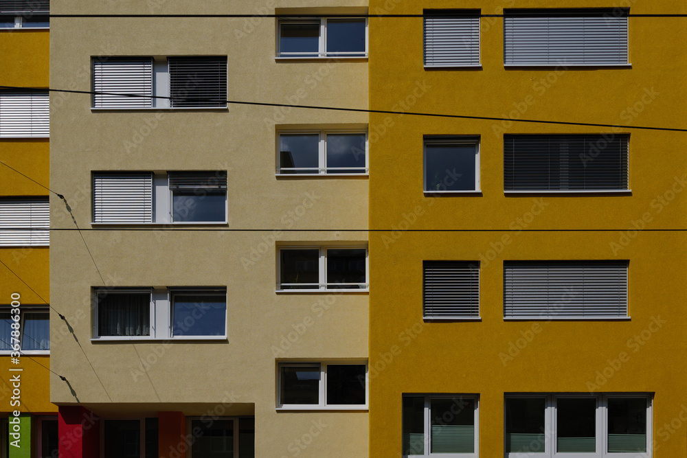 Outdoor sunny exterior front view, typical facade of modern residence or apartment in city of Europe with rectangular windows and various shade of yellow wall.