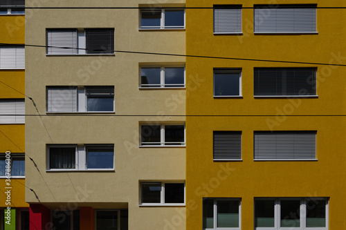 Outdoor sunny exterior front view, typical facade of modern residence or apartment in city of Europe with rectangular windows and various shade of yellow wall.