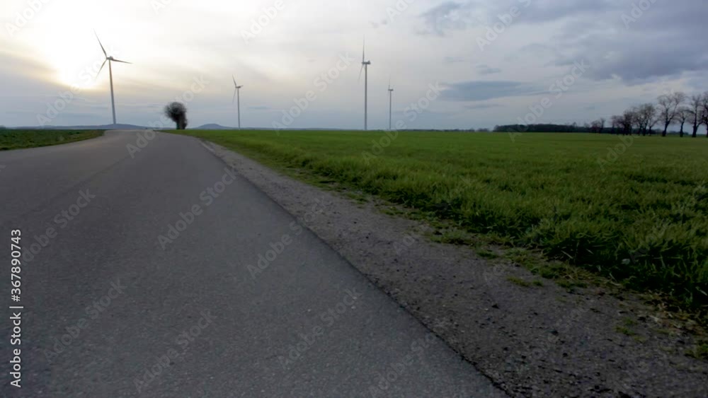 Panning shot of a windmill farm, in country fields across a road, on a cloudy evening Panning shot of a windmill farm, in country fields across a road, on a cloudy evening