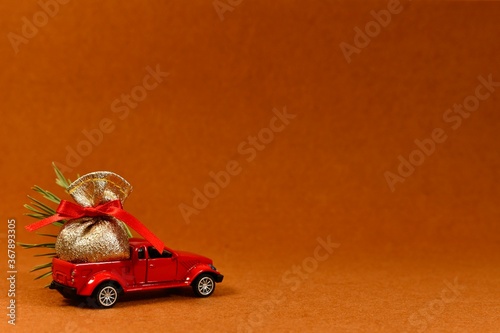 The toy pickup truck carries a bag of gifts, a Christmas tree. View front above, left on a plush teracotta background. © uly.u.v 