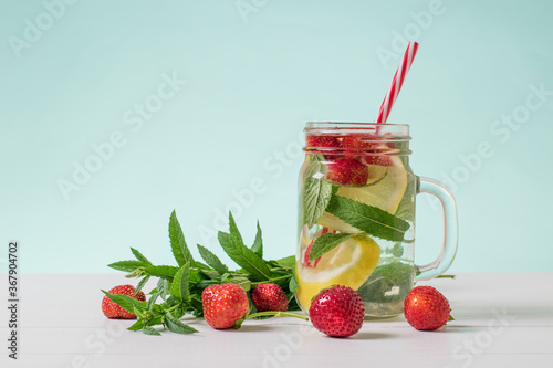 Strawberry berries and mint leaves next to a mug of cold water.