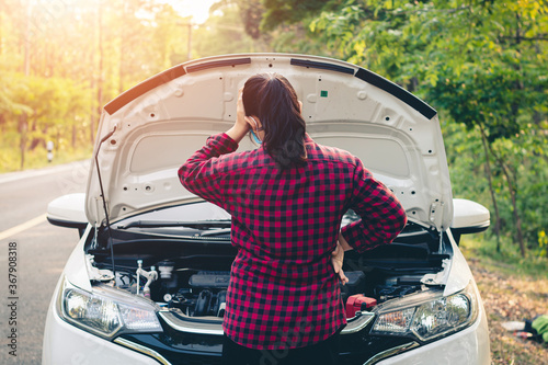 Fotografi Young woman using mobile phone while looking at broken down car on road
