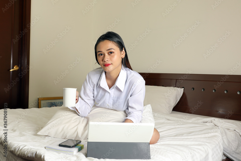 Young beautiful modern Malay woman sit on bed work study online in bedroom laptop tab coffee cup book Young beautiful modern Malay woman sit on bed work study online in bedroom laptop tab coffee cup book