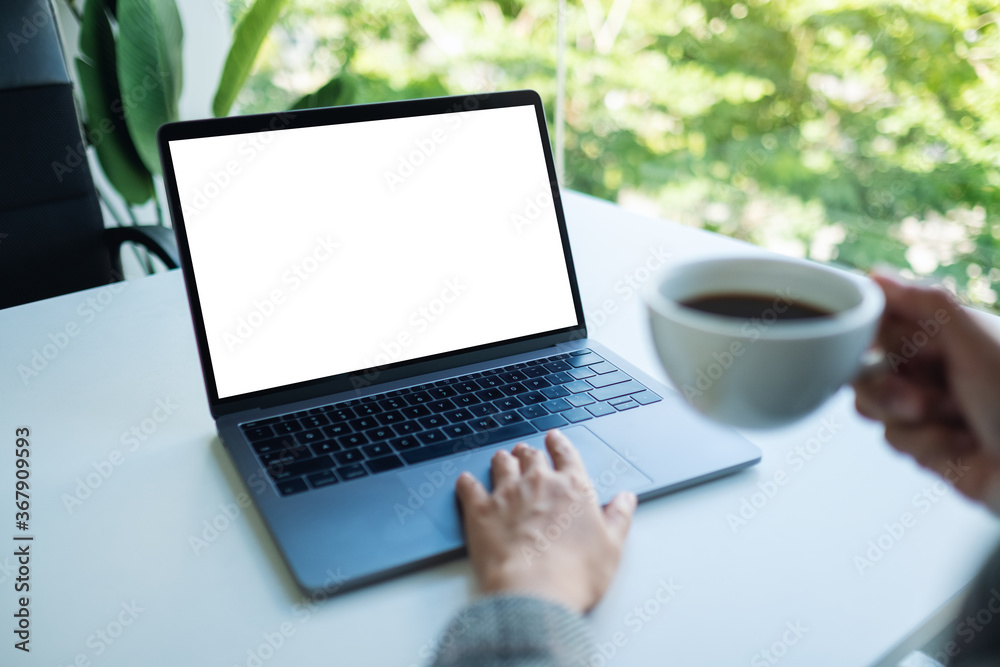 Mockup image of a businesswoman using and touching on laptop touchpad with blank white desktop screen while drinking coffee in office Mockup image of a businesswoman using and touching on laptop touchpad with blank white desktop screen while drinking coffee in office