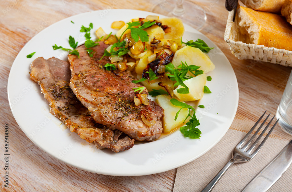 Appetizing pork steaks with side dish of boiled potatoes with fried onion and fresh greens