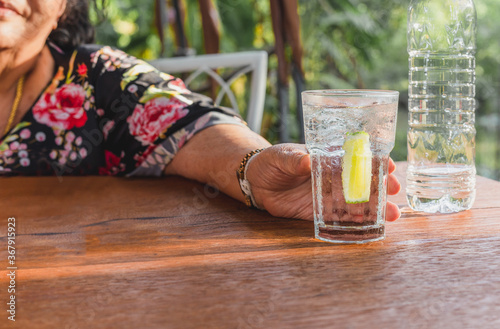 Senior woman holding fresh glass of water with lime detox drink.