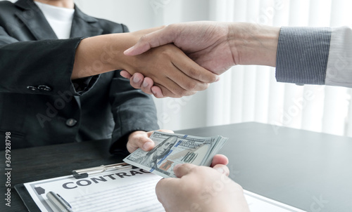 photo of Businessmen shakes hands and dollar note, sign a contract to bribe corruption in the company. The concept of bribery and corruption