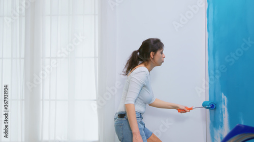 Woman decorates her home painting the wall with roller brush and dancing. Apartment redecoration and home construction while renovating and improving. Repair and decorating.