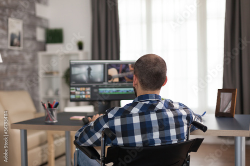 Videographer with headphones and moving handicap sitting on wheelchair working on movie. Invalid film maker doing his business online, using high technology, sitting in his apartment, working remotely photo