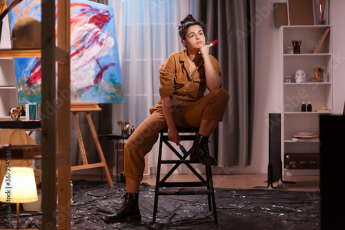 Artist resting on chair after painting a masterpiece on large canvas in art studio. Modern artwork paint on canvas, creative, contemporary and successful fine art artist drawing masterpiece