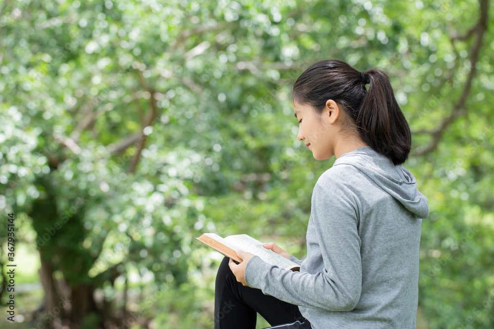 Pretty young woman reading bible in park. Reading abook.The concept of God's bible is based on faith and spirituality. Pretty young woman reading bible in park. Reading abook.The concept of God's bible is based on faith and spirituality.