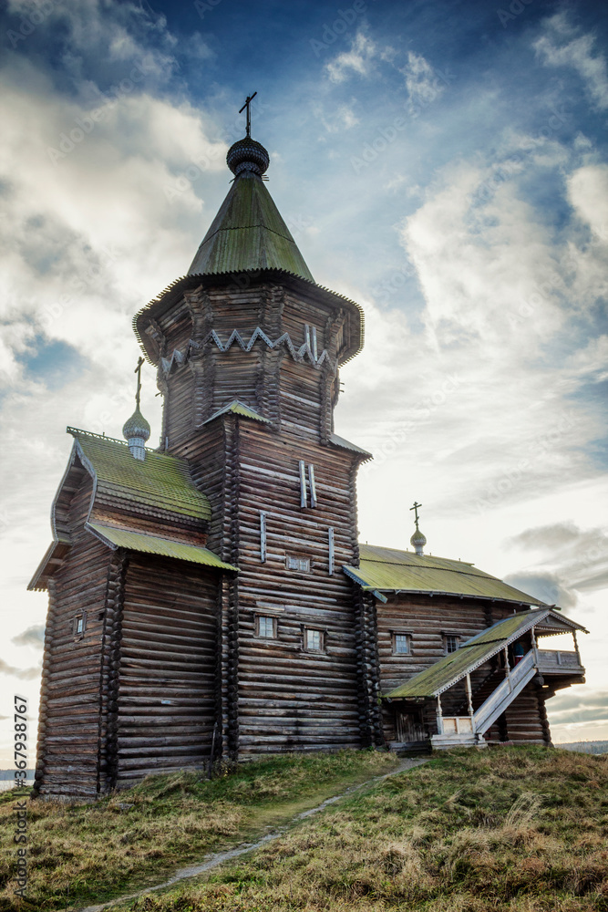 An old wooden Karelian church in a beautiful nature against the backdrop of a bright blue sky. Vertical.