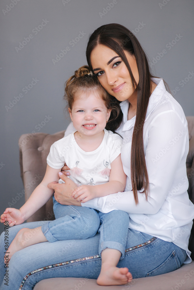 Portrait of attractive young woman with cute daughter. Mom and daughter sits on sofa in studio Portrait of attractive young woman with cute daughter. Mom and daughter sits on sofa in studio