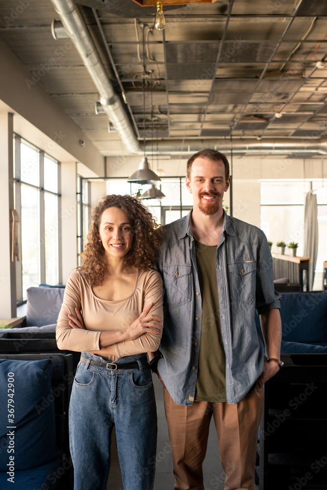 Portrait of positive young couple of cafe owners standing together in loft establishment