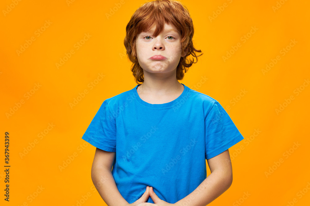 redhead boy The offended child pouted his lips blue t-shirt yellow background redhead boy The offended child pouted his lips blue t-shirt yellow background