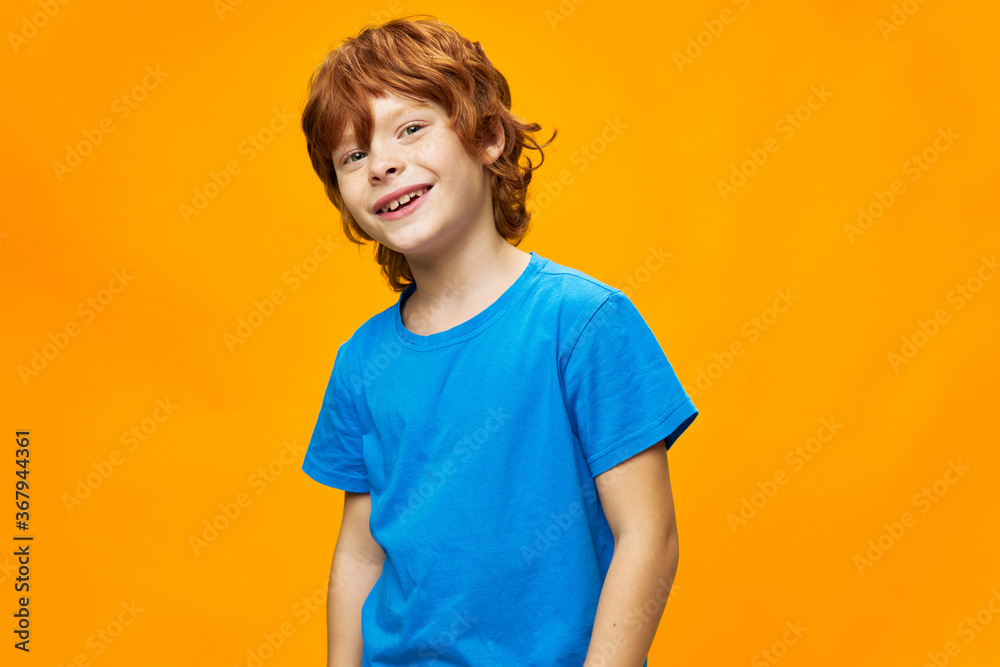 Cheerful little child boy smile side view blue t-shirt yellow background red hair Cheerful little child boy smile side view blue t-shirt yellow background red hair