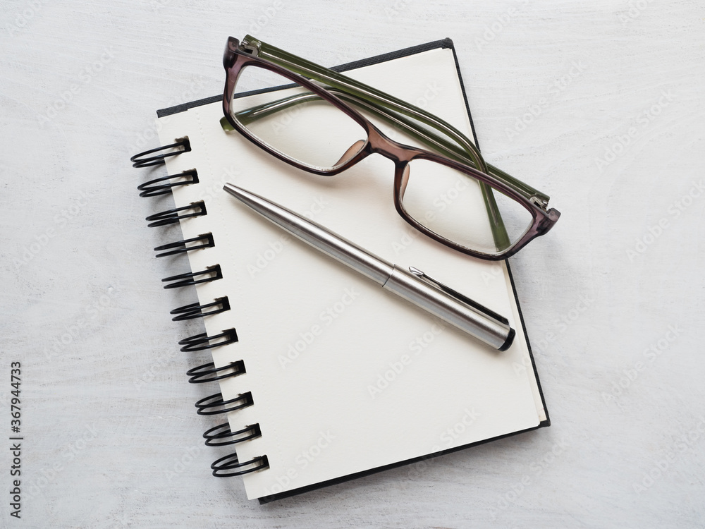 Blank notepad page, pen and glasses. Greeting card. Close-up, view from above, wooden surface. Concept of preparation for a professional holiday. Congratulations for relatives, friends and colleagues Blank notepad page, pen and glasses. Greeting card. Close-up, view from above, wooden surface. Concept of preparation for a professional holiday. Congratulations for relatives, friends and colleagues