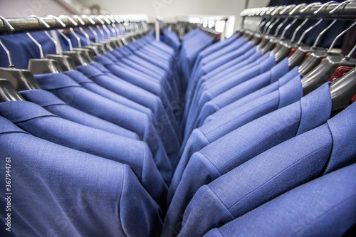 Two rows of smart blue male costumes on hangers in garment factory.
