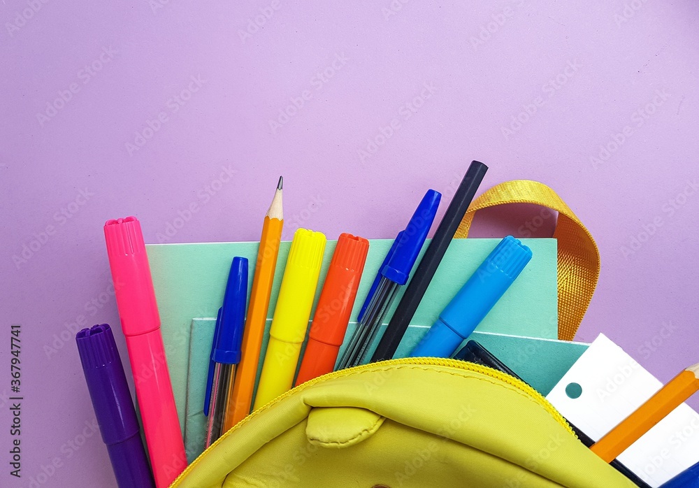 Fototapeta premium School yellow backpack with notebooks and school supplies on a purple background. Back to school.