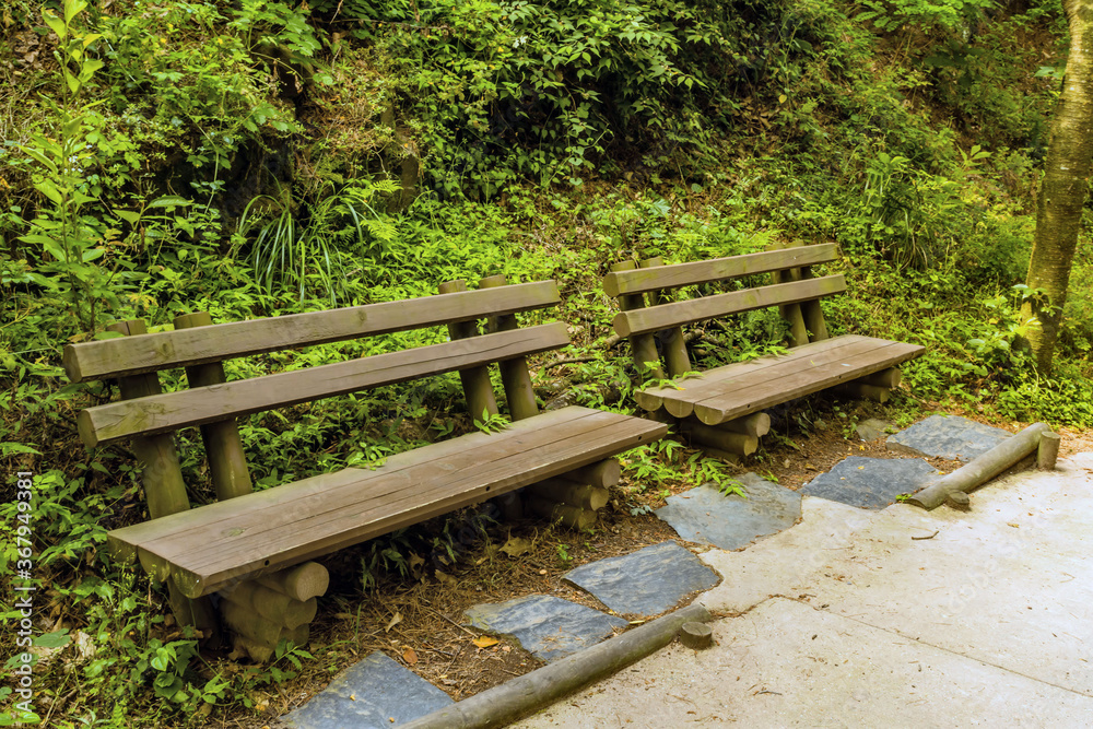Two wooden park benches beside concrete hiking trail Two wooden park benches beside concrete hiking trail