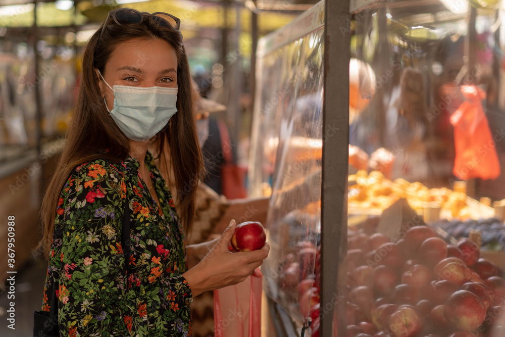 Girl buying fresh fruit at marketplace. Wearing medical face mask ageinst coronavirus pandemia outbreak. Epidemic time.