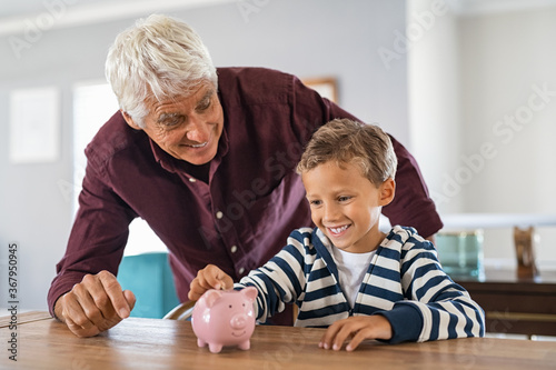 Fotografie Child and grandfather saving money in piggybank