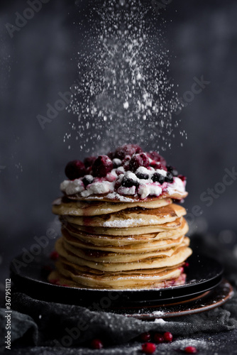 Stack of pancakes with sugar powder splashes on dark background table.