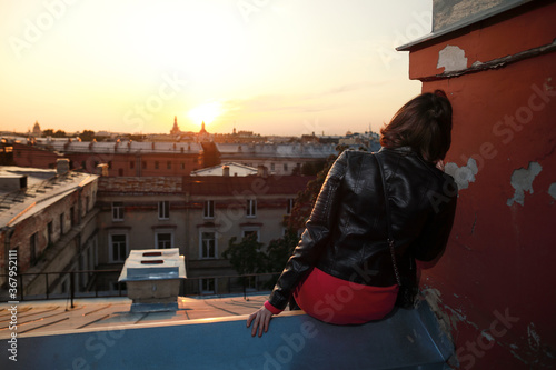 Beautiful caucasian woman siting along on rooftop on sunset background in the center city 