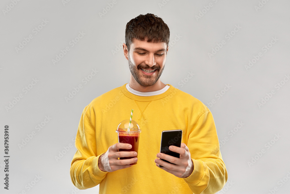 drinks and people concept - happy smiling young man with smartphone and tomato juice in takeaway plastic cup with paper straw over grey background drinks and people concept - happy smiling young man with smartphone and tomato juice in takeaway plastic cup with paper straw over grey background