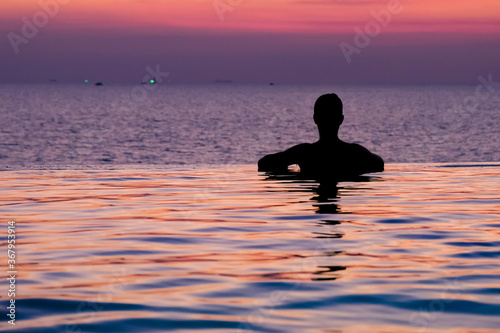 Swimming in sunset sunrise. Man swimming in infinity pool. Copy space banner. Hotel business, travel concept, travelling