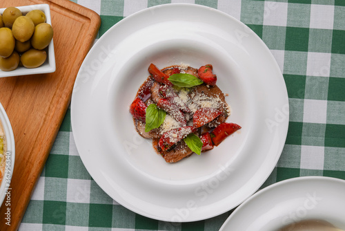 Meat in sweet and sour sauce with strawberries. Served in a white plate over green plaid tablecloth.