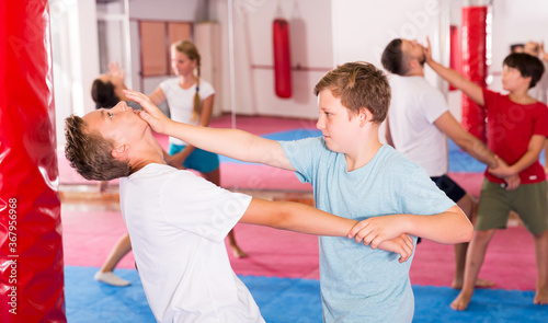 Kids with adults practicing effective techniques of self-defence in training room