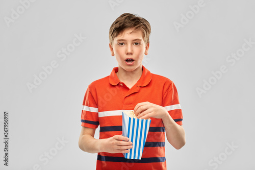 movie theater, cinema and people concept - portrait of boy eating popcorn from striped bucket over grey background photo